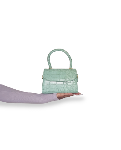 A person holding a luxury handbag with a crocodile/chameleon pattern in a mint green color.